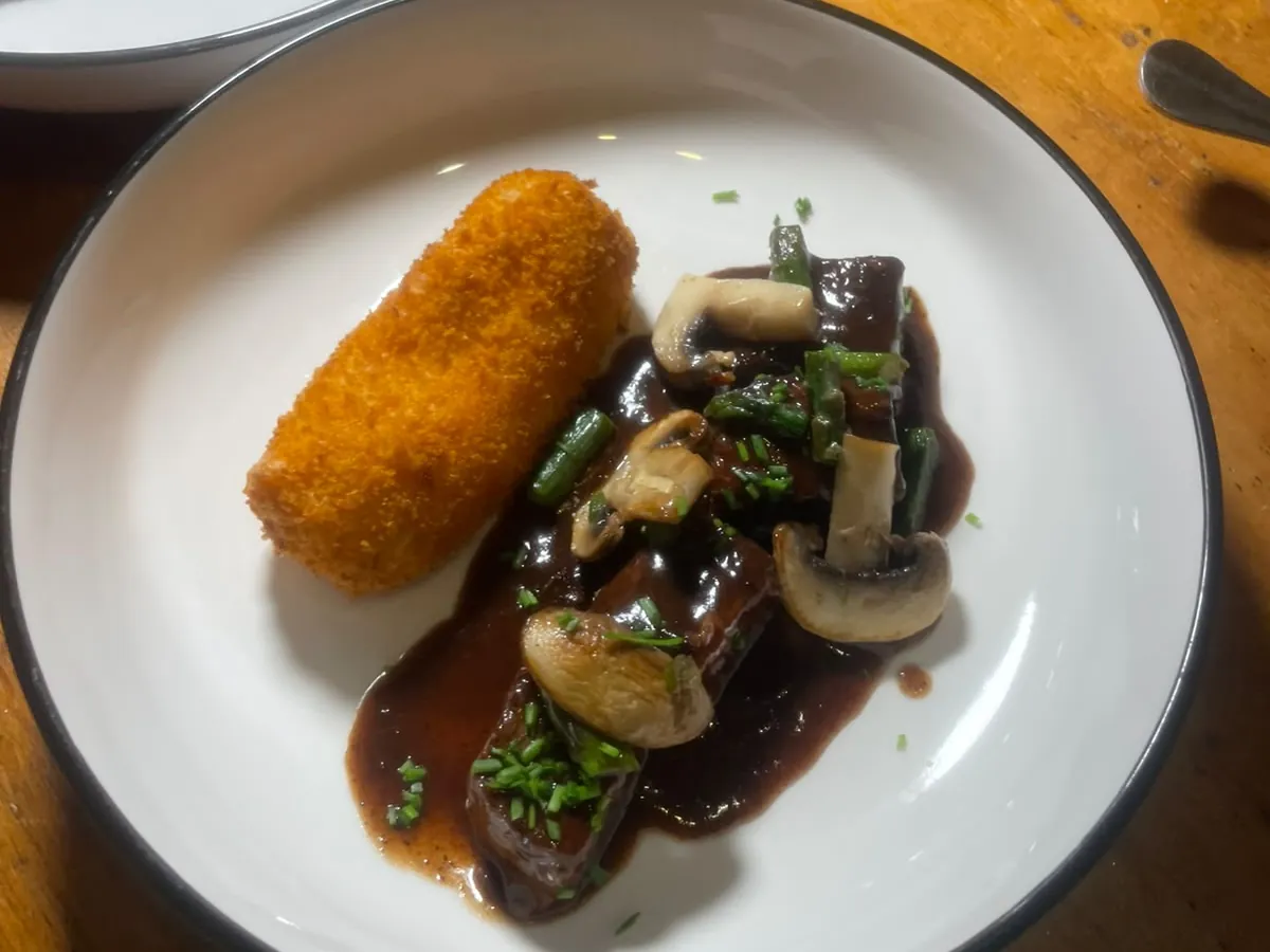 Plato de carne en salsa oscura con champiñones y una croqueta
