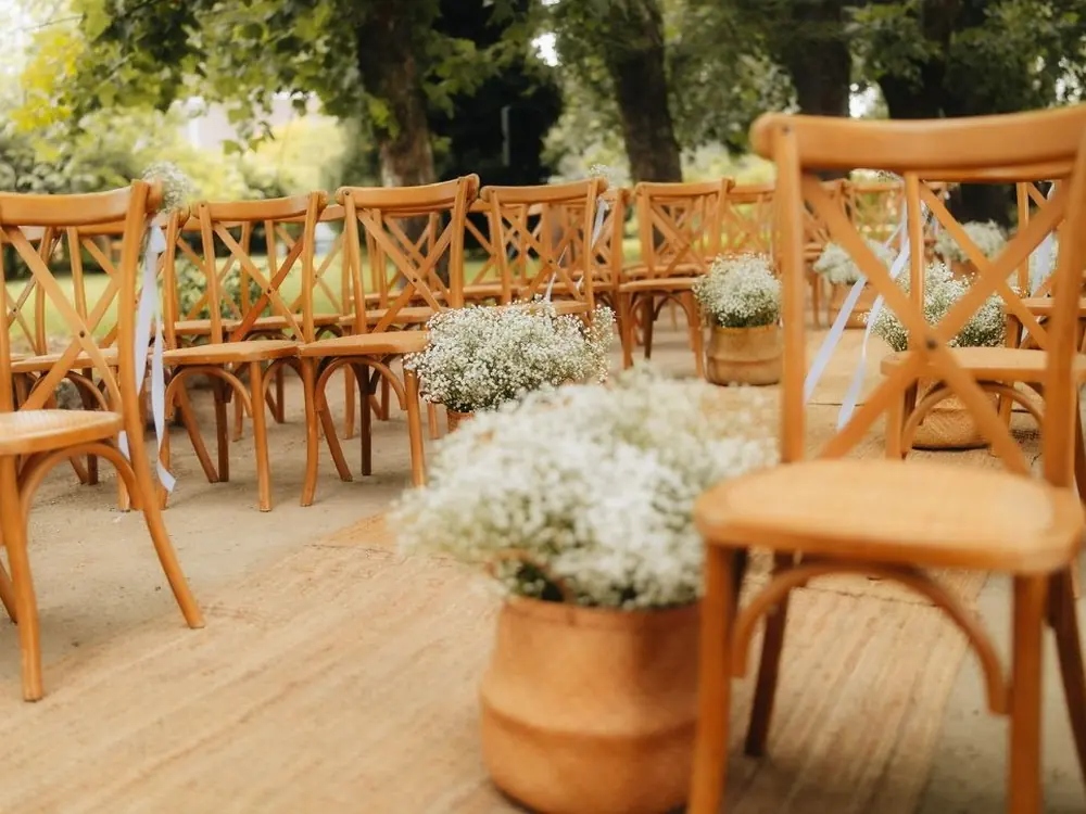 Sillas de ceremonia con arreglos de flores blancas, montadas en un jardín