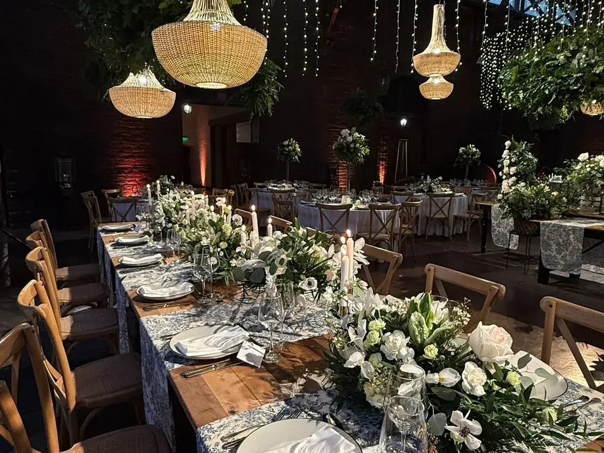 Mesa larga de matrimonio montada con flores blancas y velas bajo lámparas colgantes