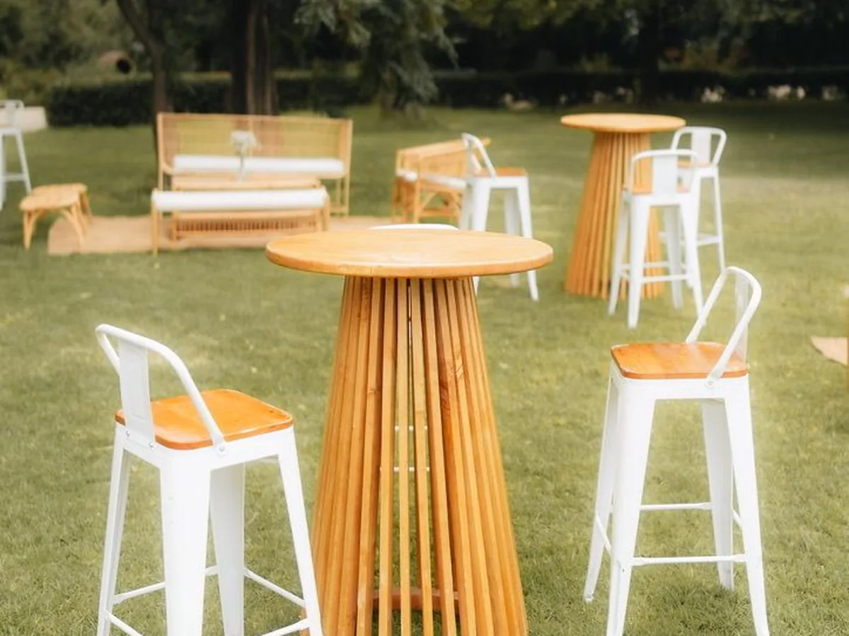 Mesas altas de madera con pisos blancos y un lounge de mimbre sobre el pasto