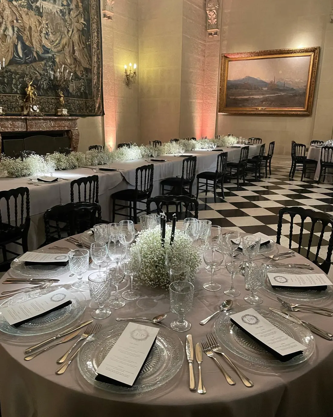 Salón montado para una cena formal: mesas redondas con mantel, cristalería y menú en cada puesto