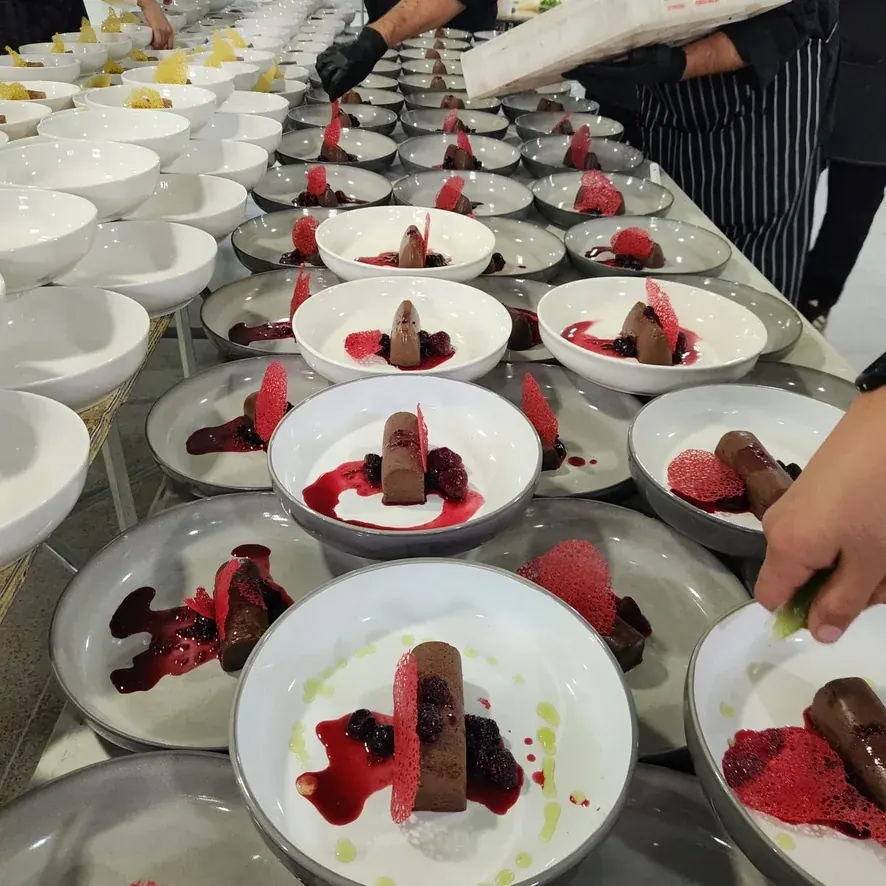 Una línea de postres emplatados en la cocina, mientras un cocinero termina el último plato