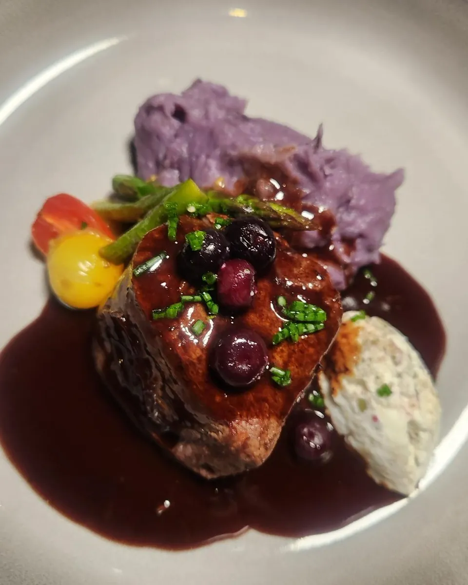 Plato de carne con puré morado, berries y salsa de vino tinto
