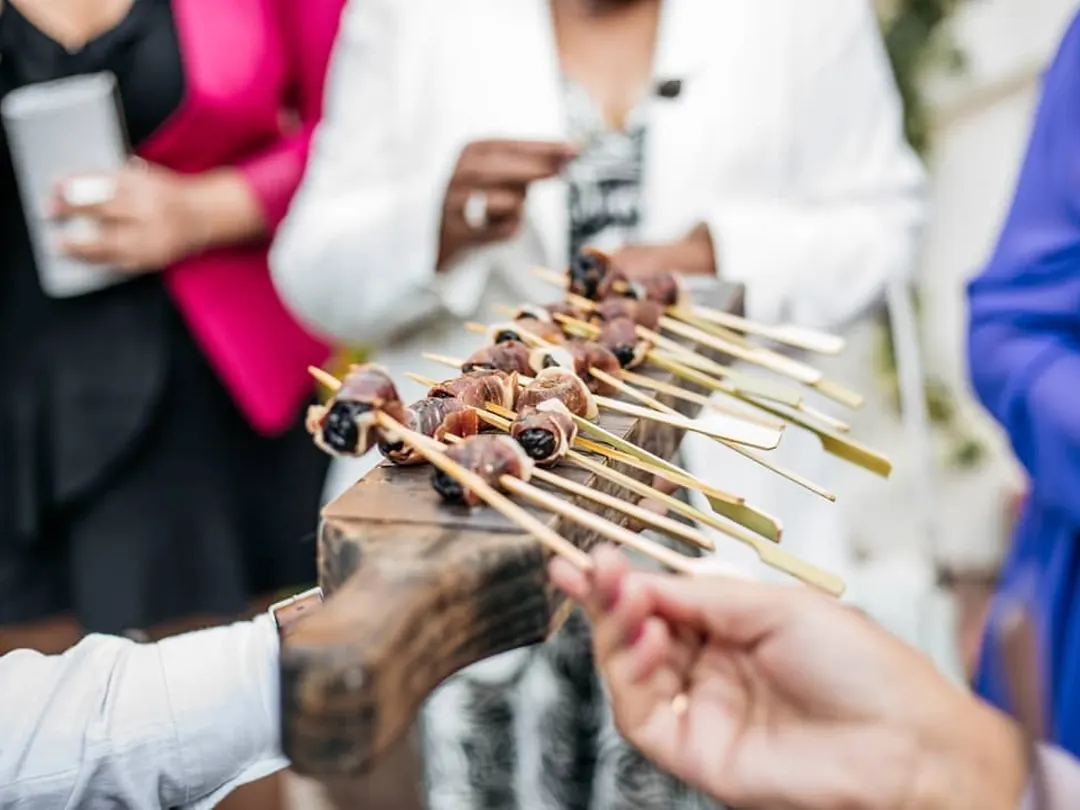 Mozo con guantes blancos pasando una bandeja de canapés entre los invitados de un evento
